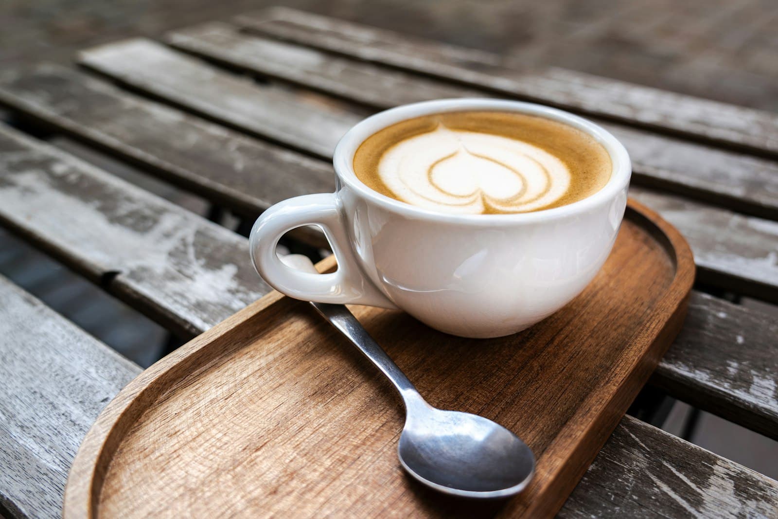 A latte with heart latte art on a wooden tray, on the porch table
